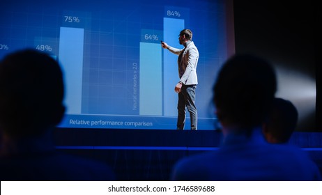 On Stage Visionary Male Speaker Presents New Technology, Uses Remote Control For Presentation, Showing Infographics, Statistics Animation On Screen. Live Event  Start-up Business Conference