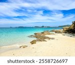 On a sunlit day, visitors enjoy the tranquil shores of Samae San Island in Thailand, where clear turquoise waters meet soft sandy beaches. The land features rocky outcrops and distant hills.