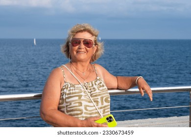 On a sunny day near the beach, an attractive elderly lady with white hair smiled as she read messages on her smart phone. The senior woman enjoyed her free time and vacation while holding the cellphon - Powered by Shutterstock