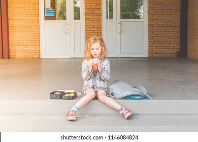 On A Sunny Day At School Break A Girl, A Child Outside, At Lunch With A Book