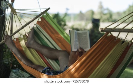 On a sunny day, young boy lying in Hammock and reading a book
