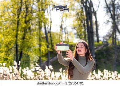 on a sunny and windy day young smiling emotional brunette receives a surprise gift delivered by quadcopter, drone delivery service, concept of modern fast delivery method