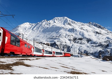 On a sunny winter day, tourists ride in a Glacier Express train and, thru the panoramic windows, enjoy the view of snowy Rossbodenstock mountain under blue clear sky, in Andermatt, Uri, Switzerland - Shutterstock ID 2343456711