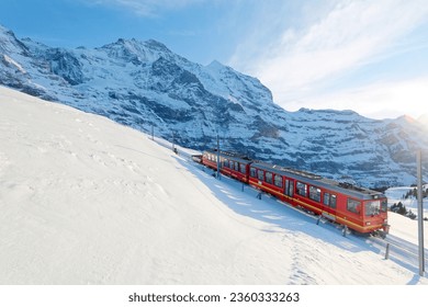 On a sunny winter day, tourists travel on a cogwheel train from Jungfraujoch (Top of Europe) to Kleine Scheidegg on the snowy hillside with Jungfrau in background, in Berner Oberland, Switzerland - Powered by Shutterstock