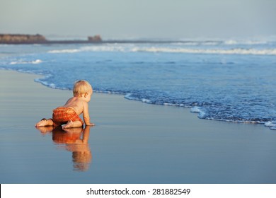 On The Sunset Beach Funny Baby Crawling On Black Wet Sand To Sea Surf For Swimming In The Waves. Family Lifestyle, And Water Activity During Summer Vacation With Child On The Tropical Bali Island