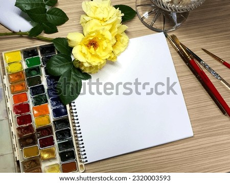 
on the table the artist's items sketchbook brushes watercolors and yellow roses