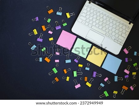 On the table on a black background there is a netbook, a computer, colored blocks for writing and copying text and colored clips.  Space for copy text, flat lay, concept of office work, webinars. 
