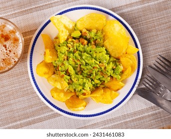 On table in cafe there is plate with traditional Mexican snack guacamole and pile of crispy potato chips. Salty and savory light repast for beer