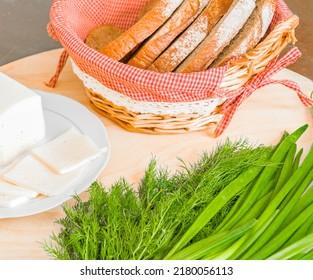 On The Table Are Cheese, Bread In A Basket, Herbs, Dill, Green Onions, A Knife On The Board