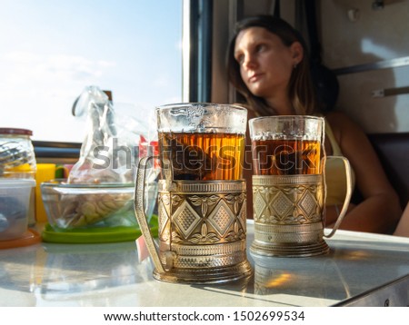 On the table in the compartment of the train are glasses with tea in metal cup holders, in the background the girl looks out the window