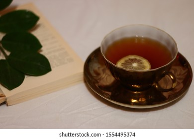 on the table is a cup with tea and a slice of lemon, a book and a green branch