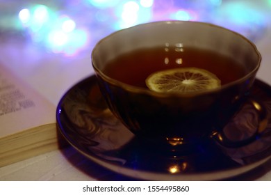 on the table is a cup with tea and a slice of lemon, a book 