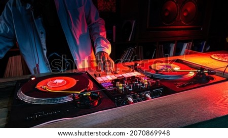 On the table, the DJ is playing a record using two vinyl turn table players playing songs in succession.