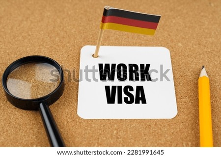On the table is the flag of Germany, a pencil, a magnifying glass and a sheet of paper with an inscription in German which translates into English as - Work Visa
