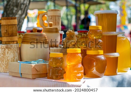 On the table are glass jars, wooden barrels and plastic containers filled with bee honey and ready to be sold at the honey fair.