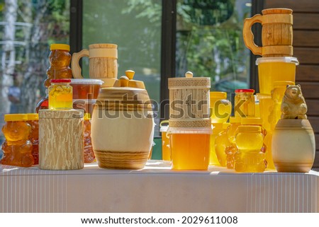 On the table are glass jars, wooden barrels and plastic containers filled with bee honey and ready to be sold at the honey fair 