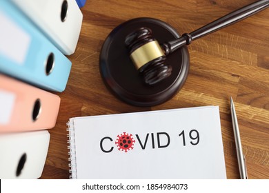 On The Table Is A Judge's Wooden Gavel And Document With The Inscription Covid -19. Coronavirus Pandemic Litigation Concept