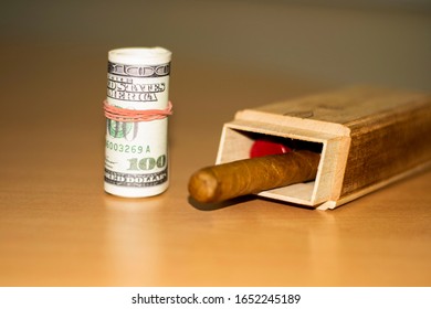 on the table lie roll bills rewound with an elastic band and a box with cigars. wooden background - Shutterstock ID 1652245189