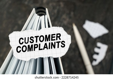 On the table is a notebook on which lies a piece of torn paper with the inscription - Customer Complaints. The pen lies outside the sharpness zone.