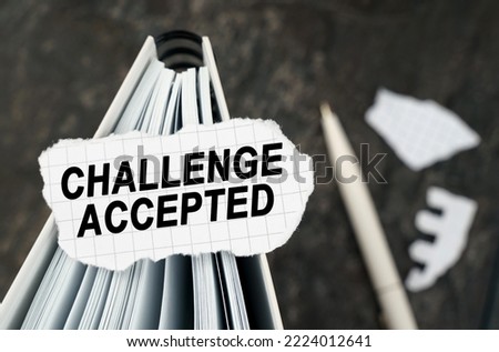 On the table is a notebook on which lies a piece of torn paper with the inscription - Challenge Accepted. The pen lies outside the sharpness zone.