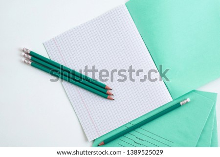 On the table is an open notebook in a cage. Pencils next to the school notebook. Notebook for school