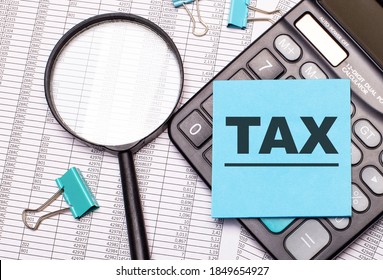 On the table are reports, a magnifying glass, a calculator, and a blue note sticker with the word TAX. Business concept