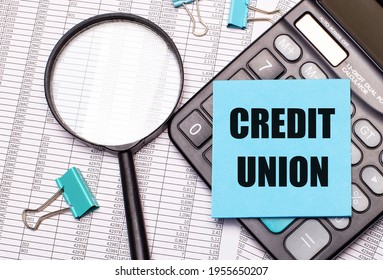 On the table are reports, a magnifying glass, a calculator, and a blue note sticker with the words CREDIT UNION. Business concept