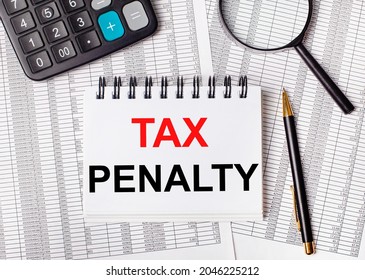 On the table are reports, a magnifying glass, a calculator, a pen, and a white notebook with the text TAX PENALTY. Business concept