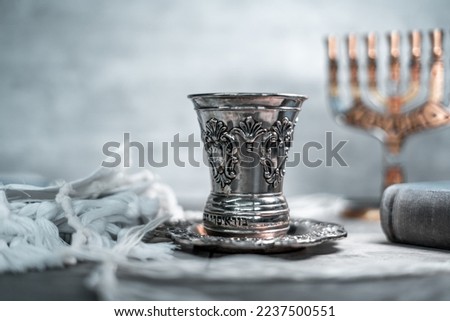 On the table is a silver glass for kiddush with shabbat wine, next to the menorah, there is a folded tallit and siddur (jewish prayer book). Jewish traditions and religion (124)