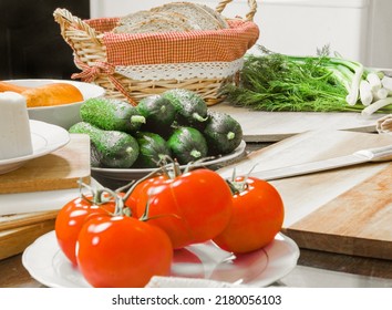 On The Table Are Tomatoes, Cucumbers, Carrots, Cheese, Bread In A Basket, Herbs, Dill, Green Onions, A Knife On The Board