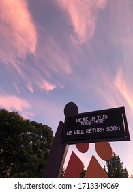 We’re On This Together , We Will Return Soon . A Light Up Sign With A Sky With Pink Clouds