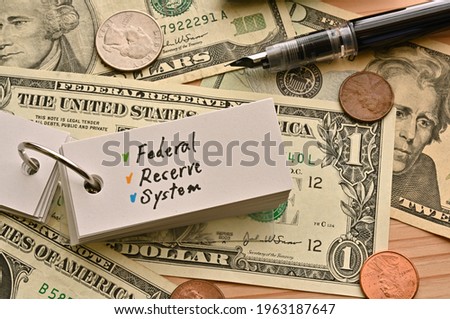 On top of the dollar bills on the table, there is a word book with the financial term Federal Reserve System written on it.