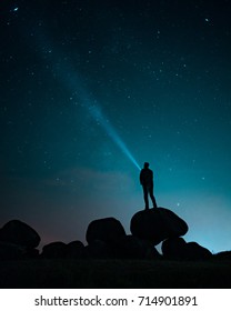 On top of a 'hunebed' in the Netherlands a man is standing in the night watching the sky. His beam is shining back at the stars while gazing into the void. 