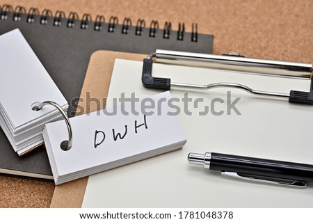 On top of the notebook and clipboard is a wordbook and pen with the word DWH written on it. It means Data WareHouse.