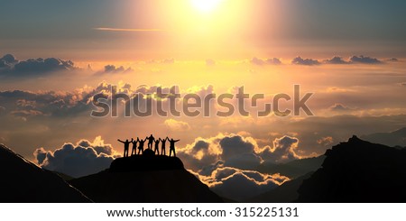 On the top of the world together. A group of people stands on a hill over the beautiful cloudscape.