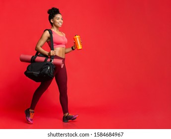 On A Way To Gym. Beautiful Afro Woman With Yoga Mat, Sporty Bag And Shaker In Hand Going Towards Copy Space