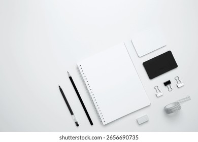 On a white background, an empty mock up notebook, white and black cards, monochrome stationery items arranged neatly
