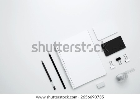 On a white background, an empty mock up notebook, white and black cards, monochrome stationery items arranged neatly