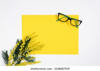 On a white background flat lay with a yellow mimosa flower, glasses, a female floral desktop. The concept of a stylish spring morning. top view and copy space