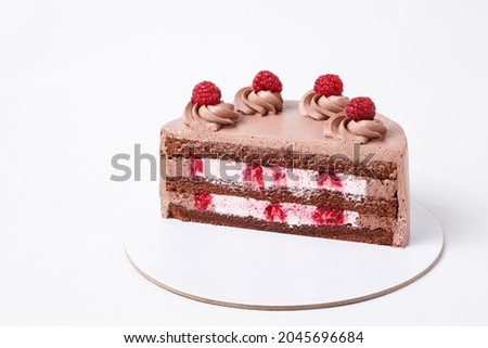 On a white background, a sweet pastry cake is cut in half, the cake is cut in half, the filling and the raspberry berry are visible. Chocolate sponge cake and white cream. Demonstration of products in
