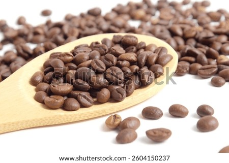 On a white background there are many scattered coffee beans on a wooden spoon.