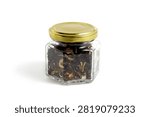 On a white background there is one glass jar of black tea with dry leaves and dried fruits.