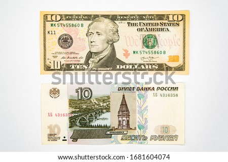 On a white background are two paper bills of 10 US dollars and another 10 Russian rubles