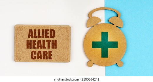 On The White And Blue Surface Are An Alarm Clock And A Sign With The Inscription - Allied Health Care