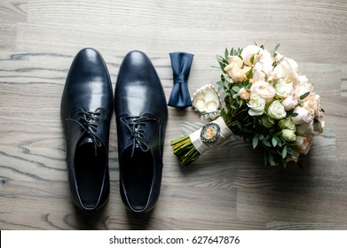 On The White Floor Are Black Men's Shoes, A Bouquet Of Flowers, A Man's Bowtie And A Watch. Close Up Photo, Details Of The Wedding.