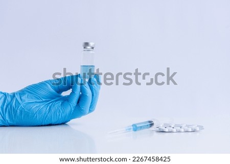 On white isolated background, hands of doctor in medical blue gloves hold ampoule vaccine against virus coronovirus. Syringe with antidote, pain pills. Fighting pandemic, epidemic. Mock up, copy space