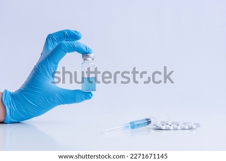On white isolated background, hands of doctor in medical blue gloves hold ampoule vaccine against virus coronovirus. Syringe with antidote, pain pills. Fighting pandemic, epidemic. Mock up, copy space