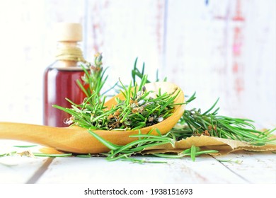 On white rustic table, rosemary leaves in wooden spoon and glass jar.