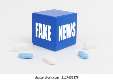 On a white surface are pills and a blue cube that says - FAKE NEWS