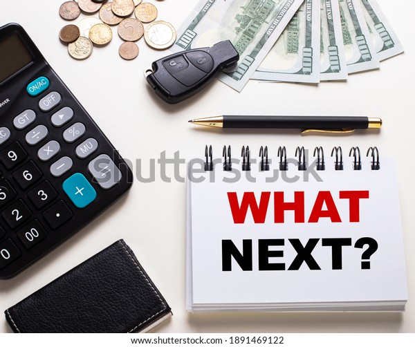 On a white table\
is a calculator, car key, cash, a pen and a notebook with the\
inscription question WHAT\
NEXT